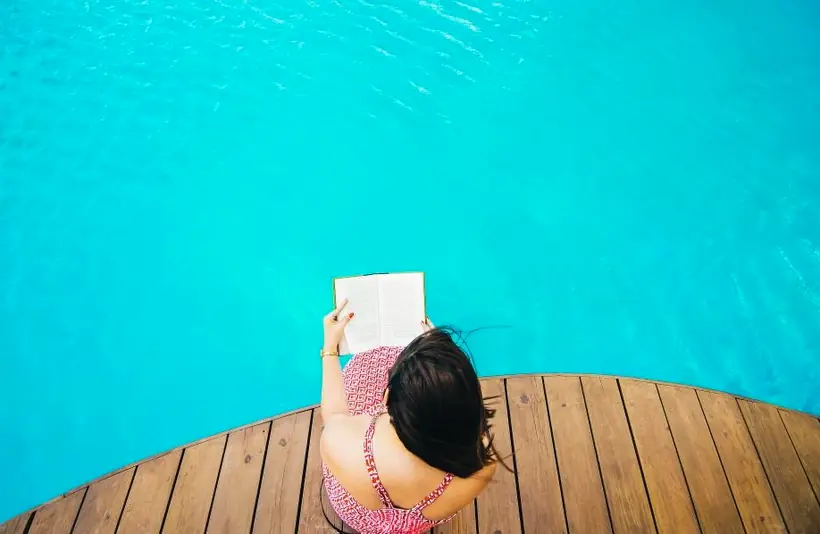 A swimmer resting on the pool deck with a book